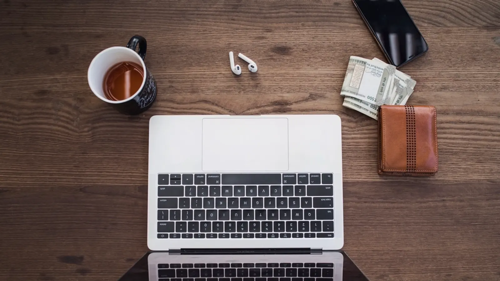 Laptop von oben auf einem Holztisch mit Tasse und Geldbörse