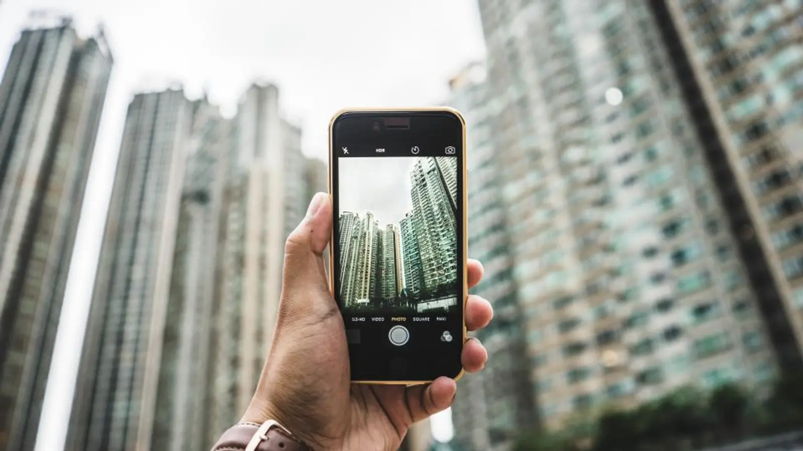 A hand holding a phone up in front of tall buildings
