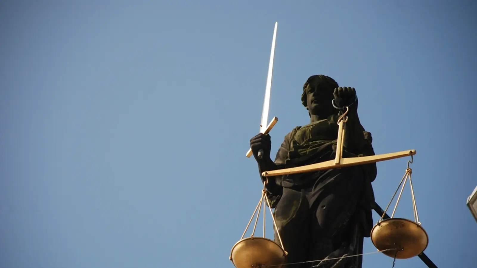 Statua della Giustizia con spada e bilancia contro il cielo