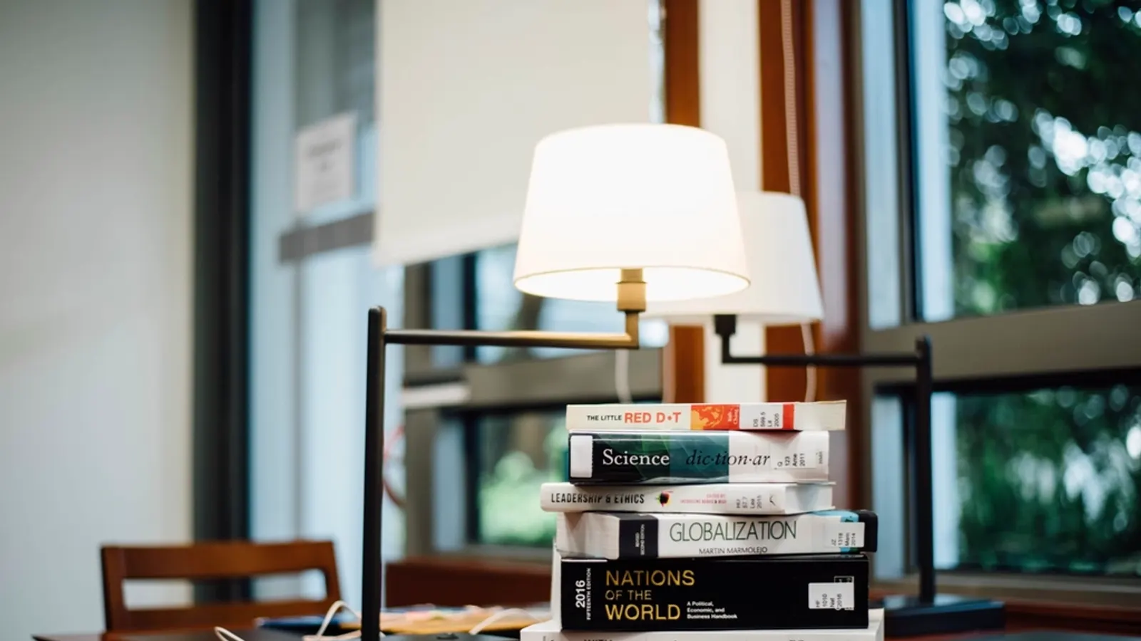 Stack of books on a table beside a reading lamp