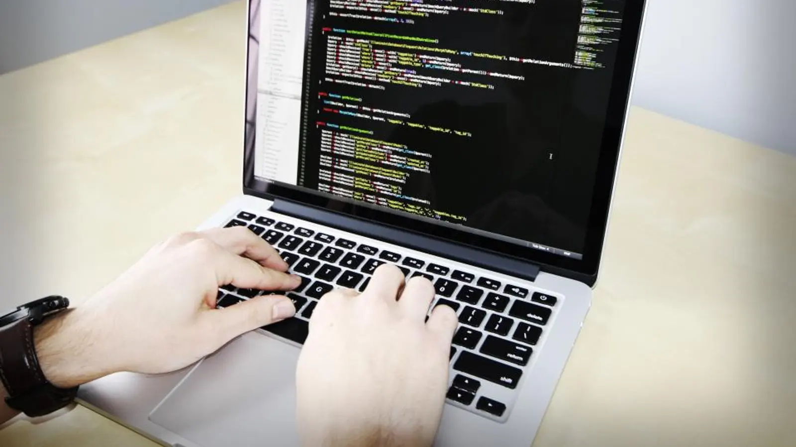 Hands typing on a laptop showing code on screen