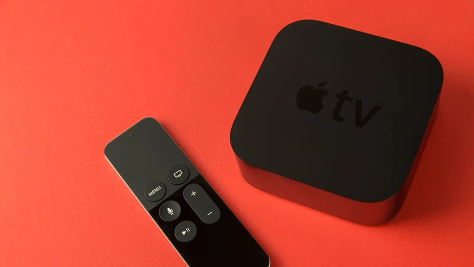 An Apple TV box and Siri Remote on a red surface