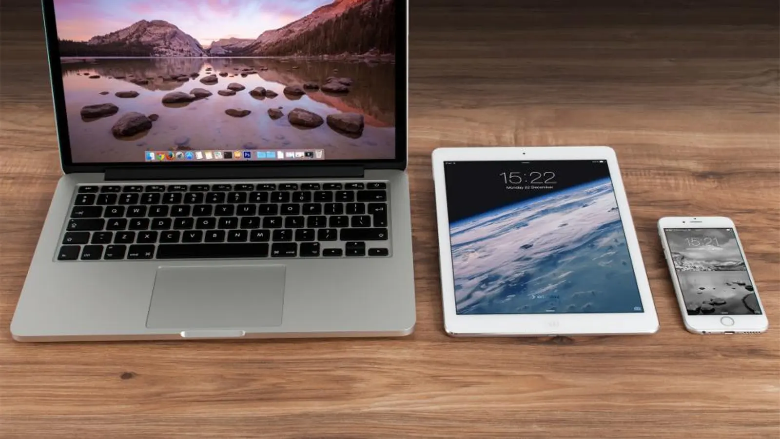 A MacBook, iPad and iPhone laid out on a wooden desk