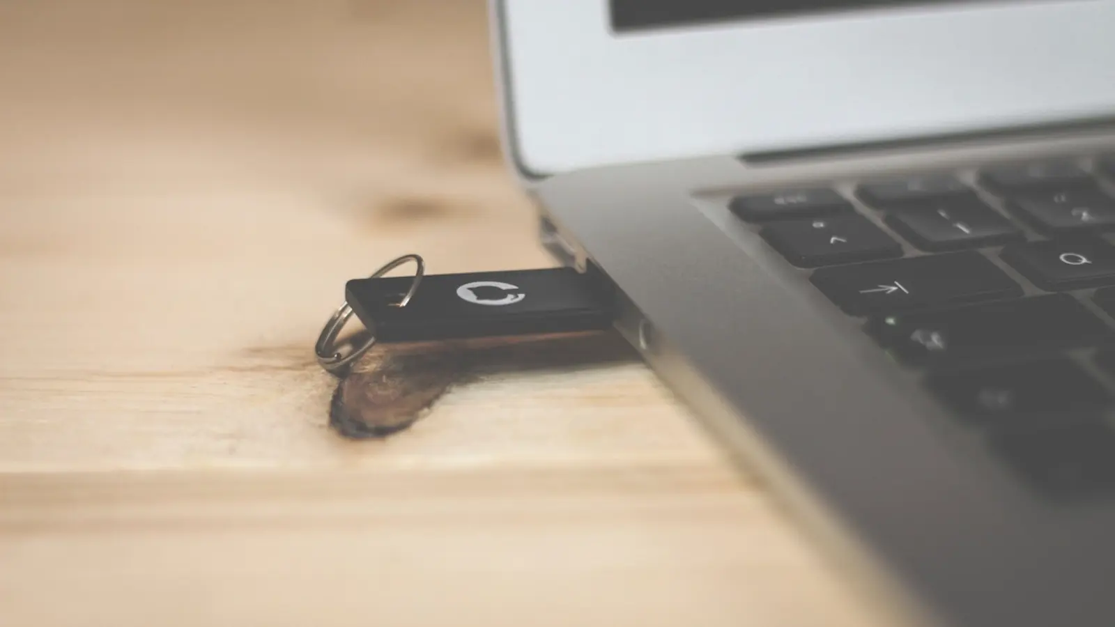 USB-Stick in einem Laptop auf einem hellen Holztisch