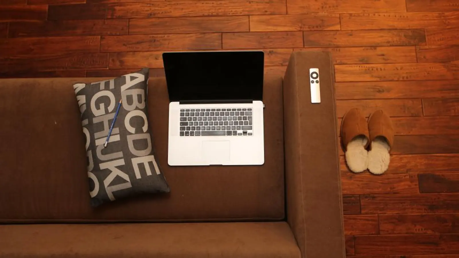 Laptop auf einem braunen Sofa neben einem Kissen
