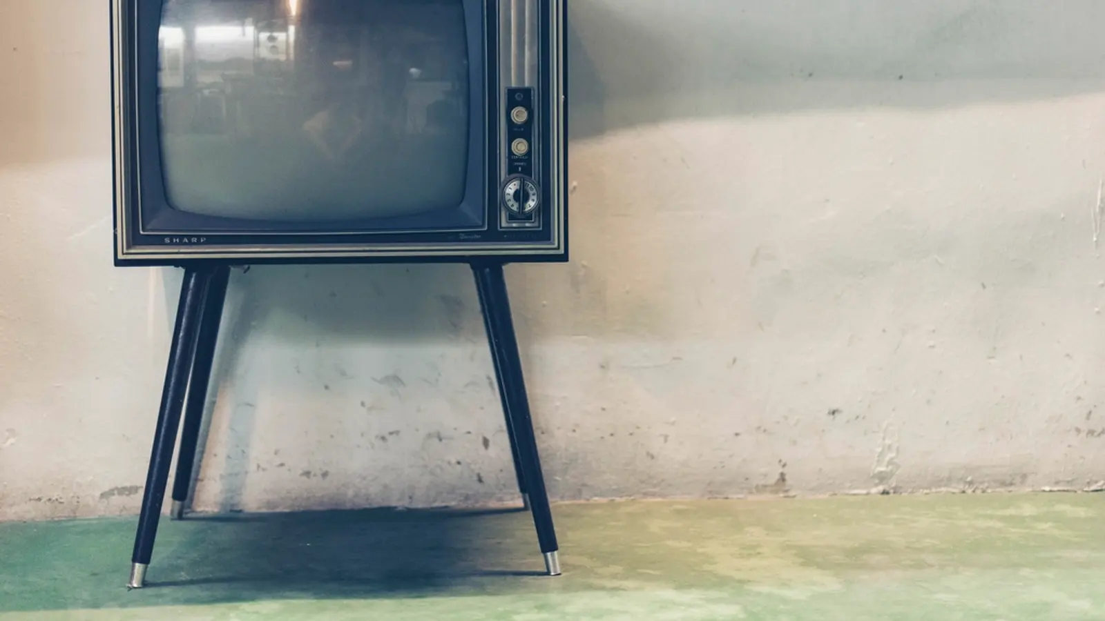 Televisor antiguo sobre patas junto a una pared desconchada