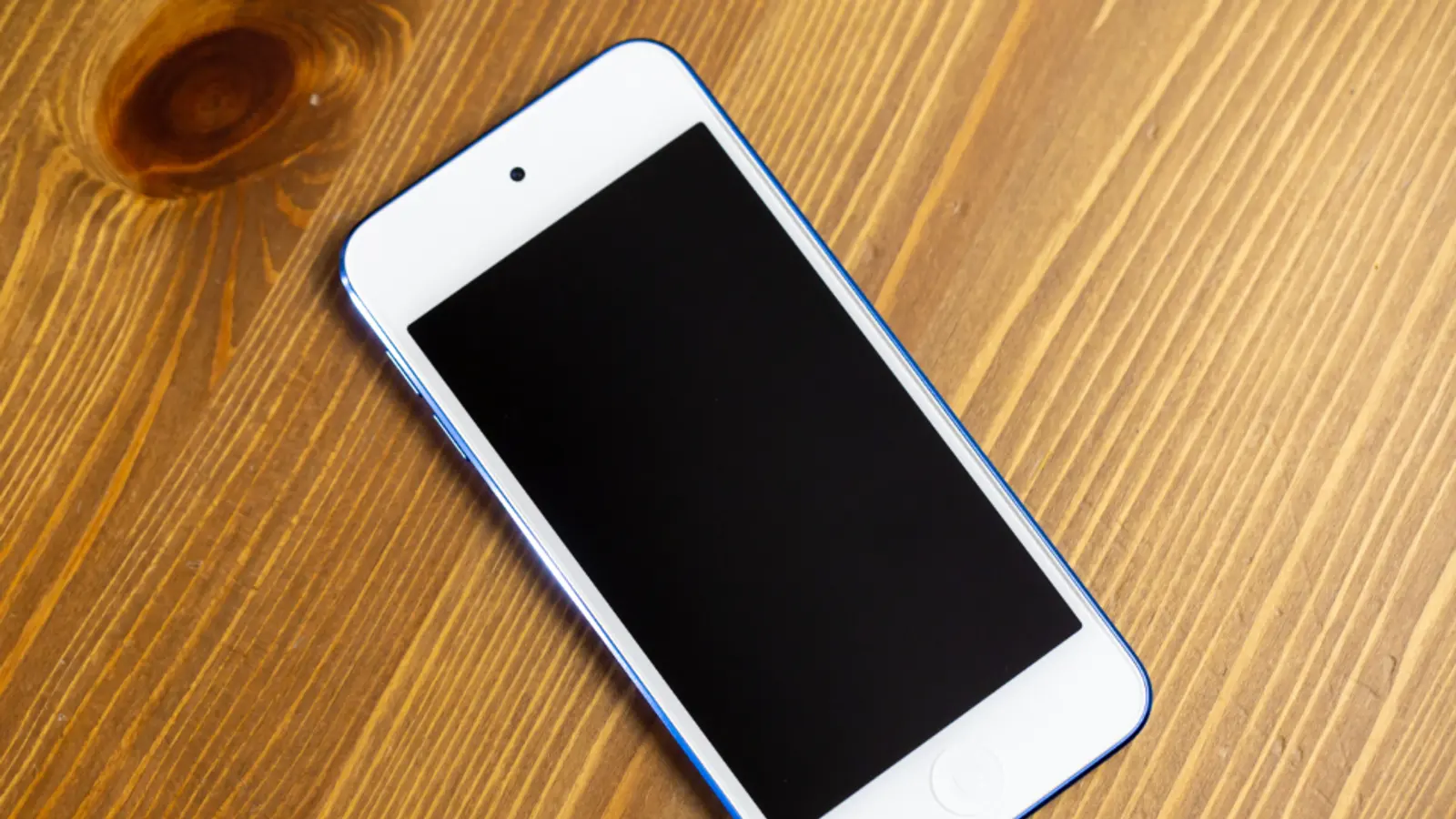 Teléfono móvil blanco con la pantalla apagada sobre una mesa de madera