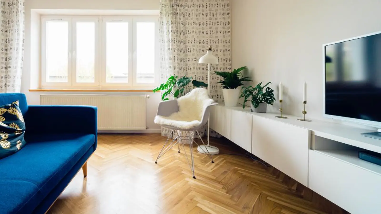 Salón luminoso con sofá azul y un televisor sobre un mueble blanco