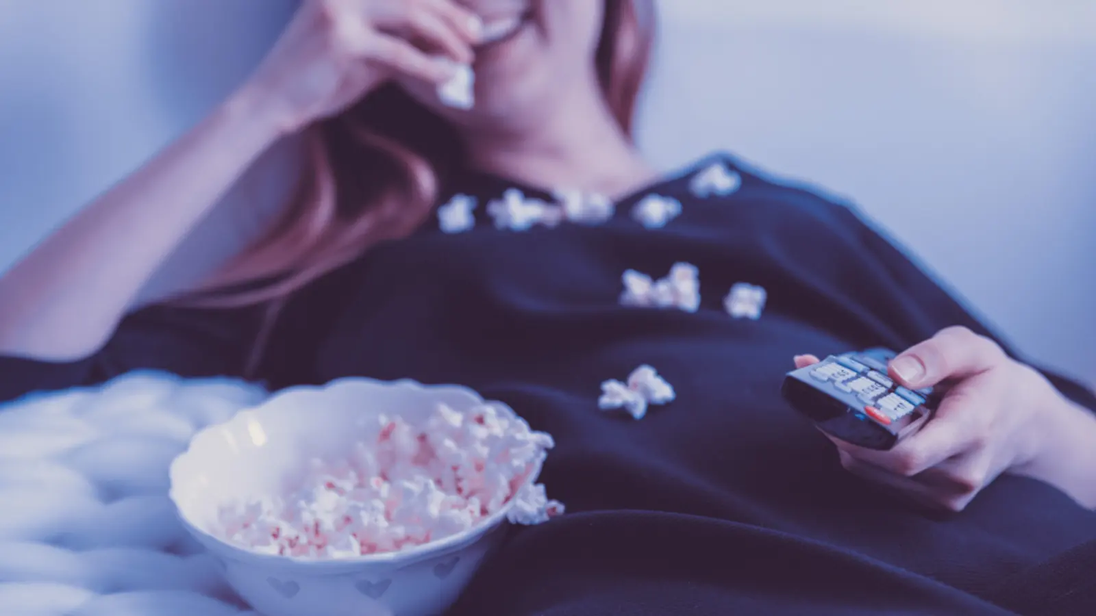 Personne allongée avec un bol de pop-corn et une télécommande