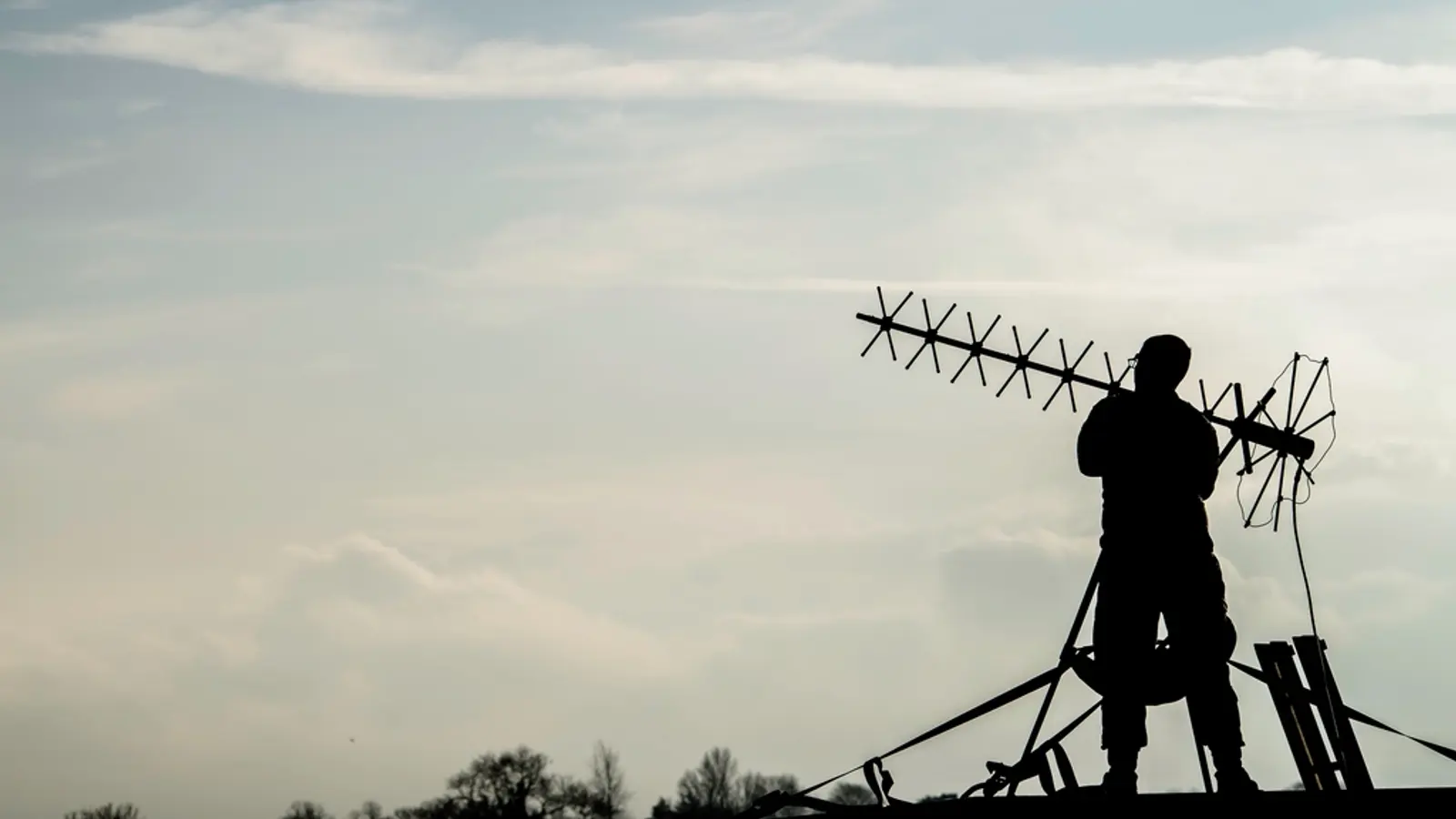 Silhouette d'une personne portant une antenne râteau sur un toit