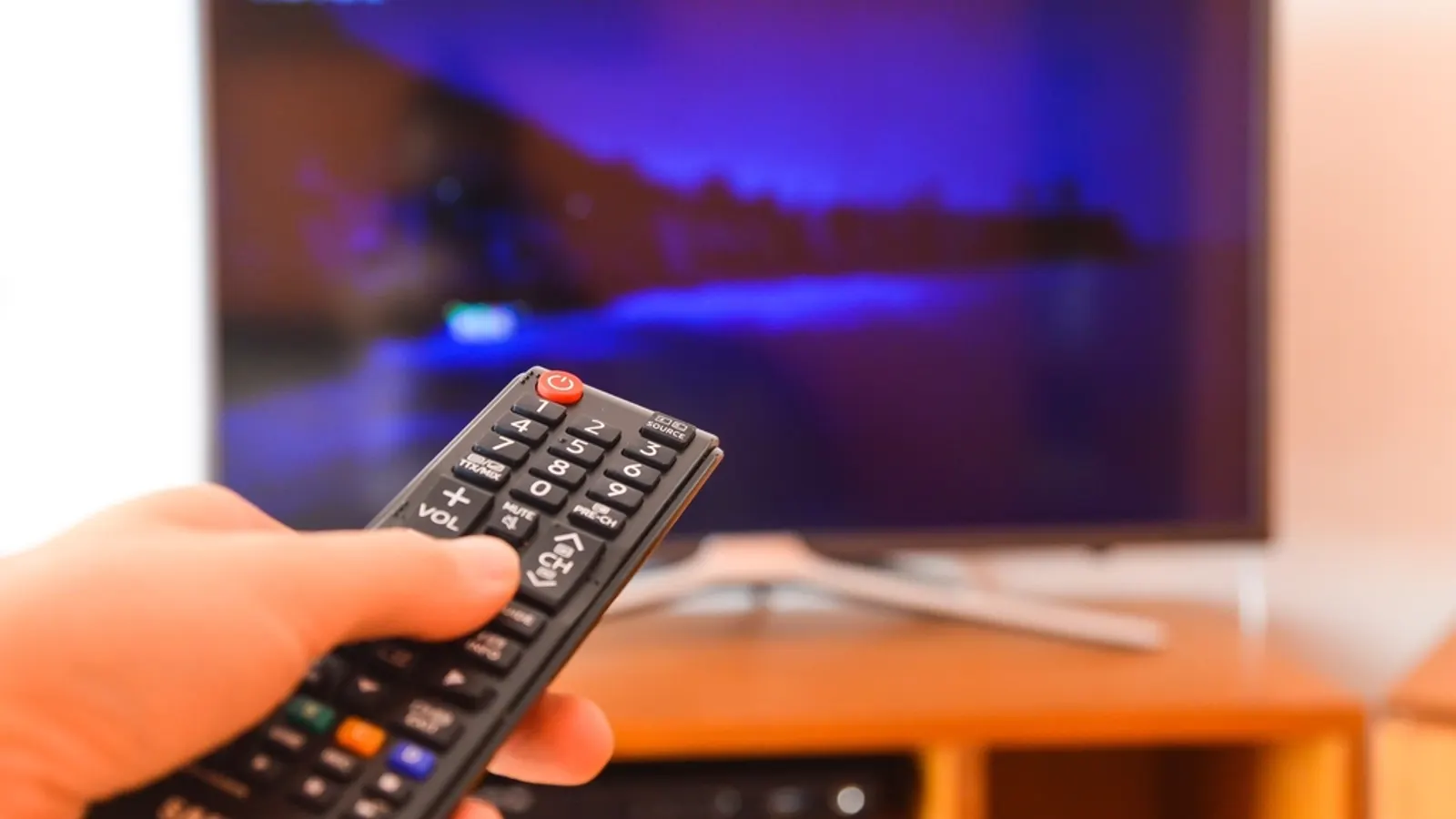 Hand pointing a remote control at a smart TV on a wooden stand