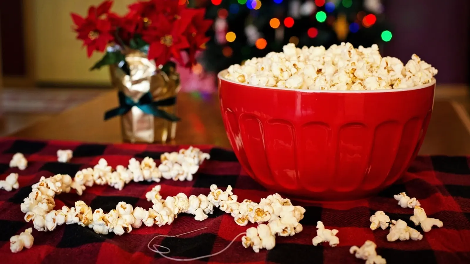 A red bowl of popcorn on a tartan tablecloth with festive lights behind