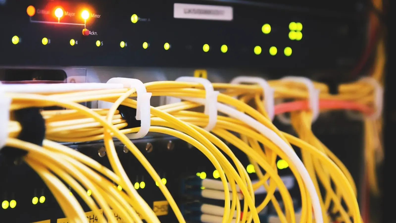 Yellow fibre cables plugged into a switch with glowing lights