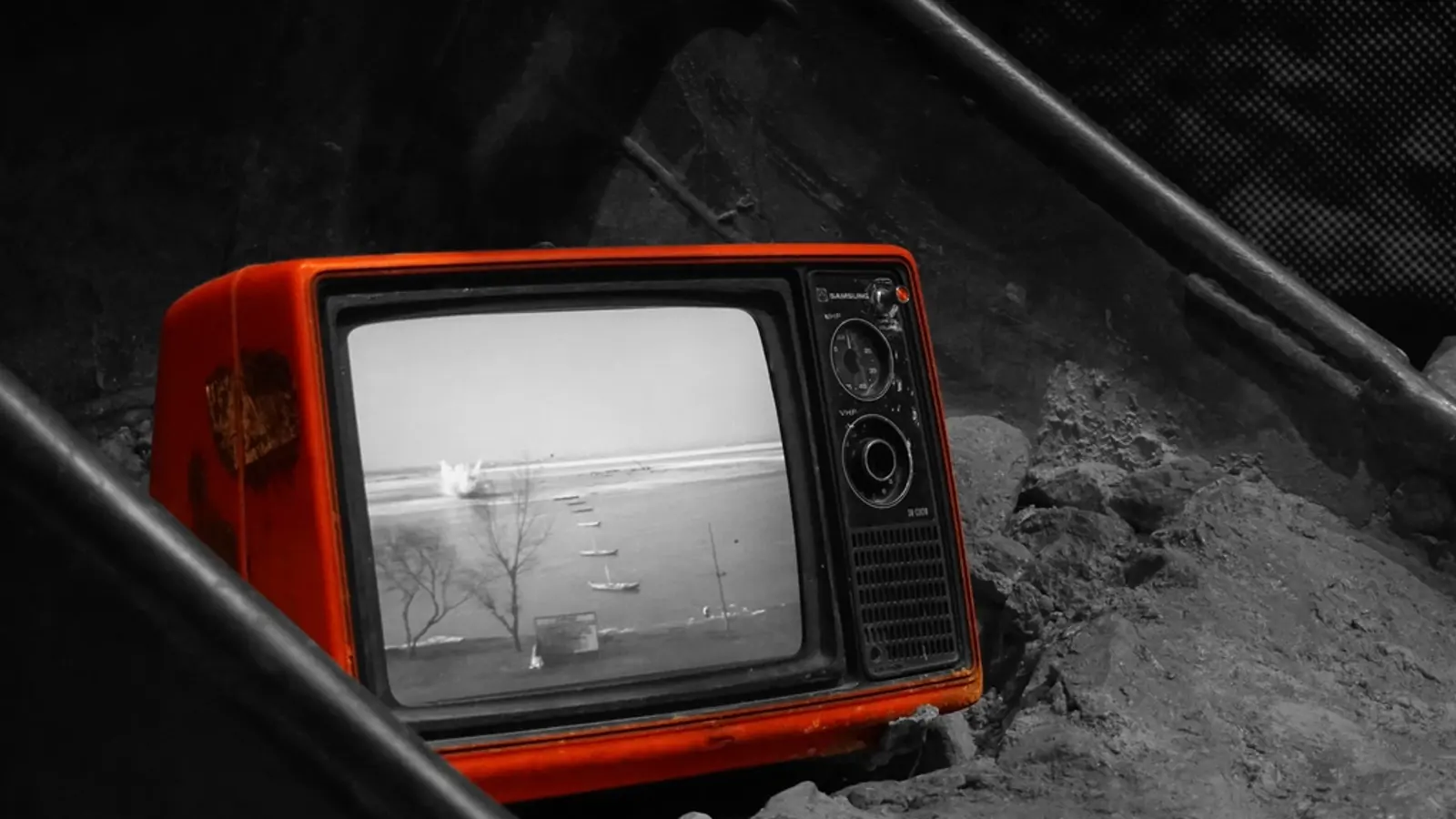 An old orange television set showing static, sitting on rubble