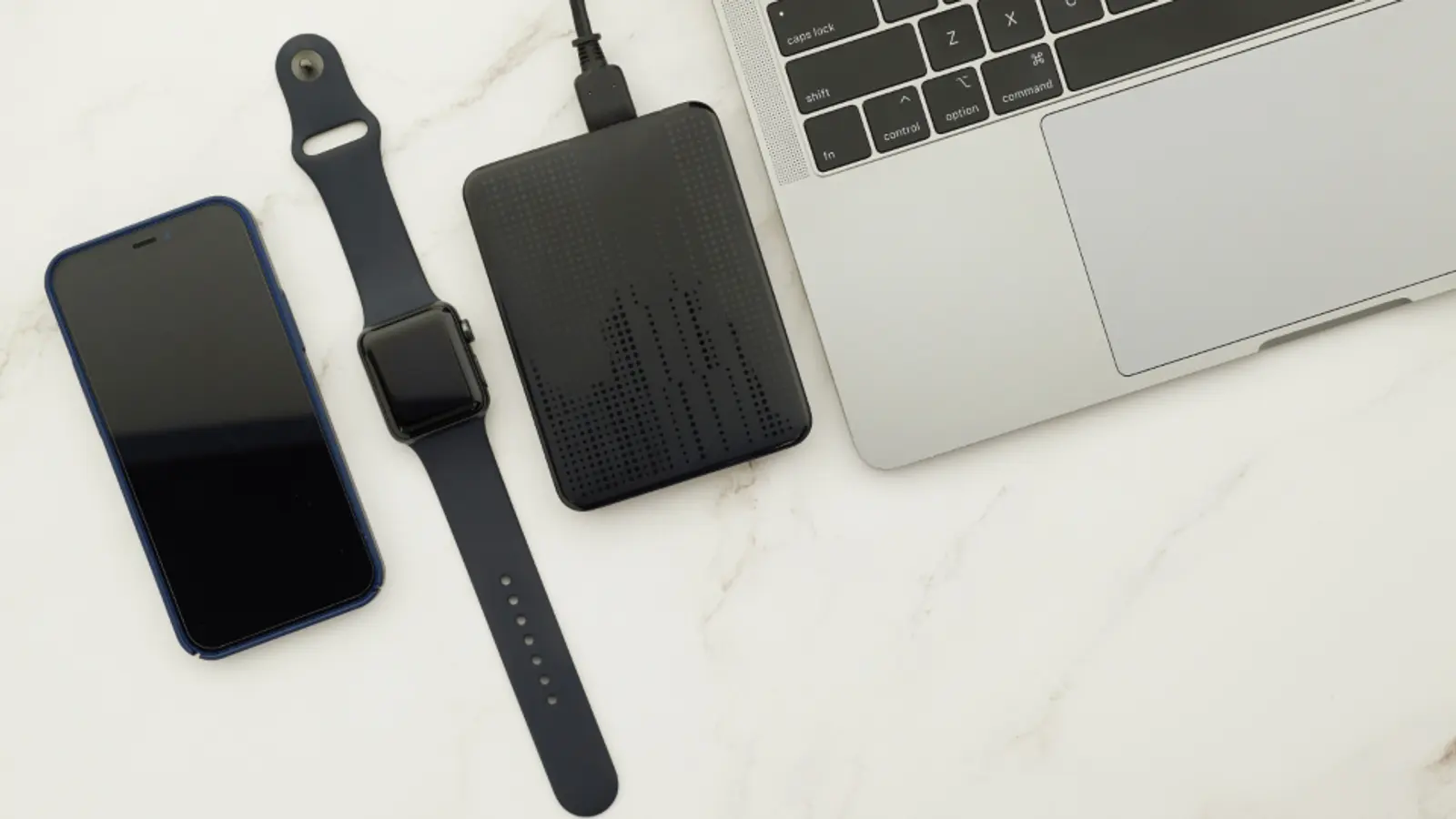 An external hard drive next to a phone and smartwatch on a marble desk
