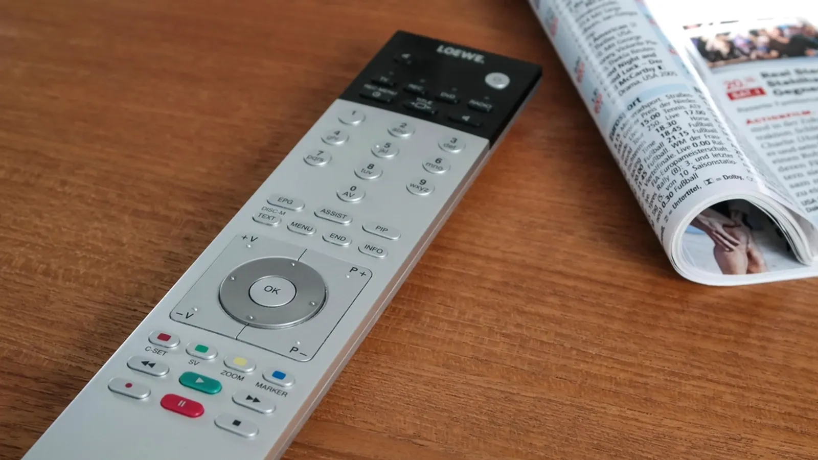 Silver TV remote control on a wooden table next to a magazine