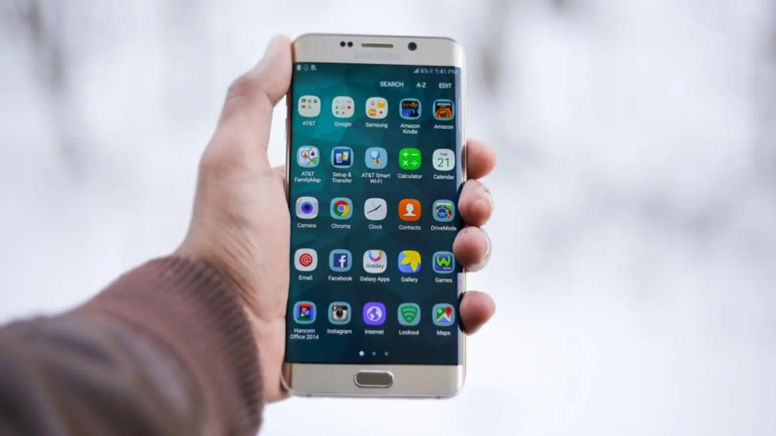 A hand holding an Android phone showing app icons