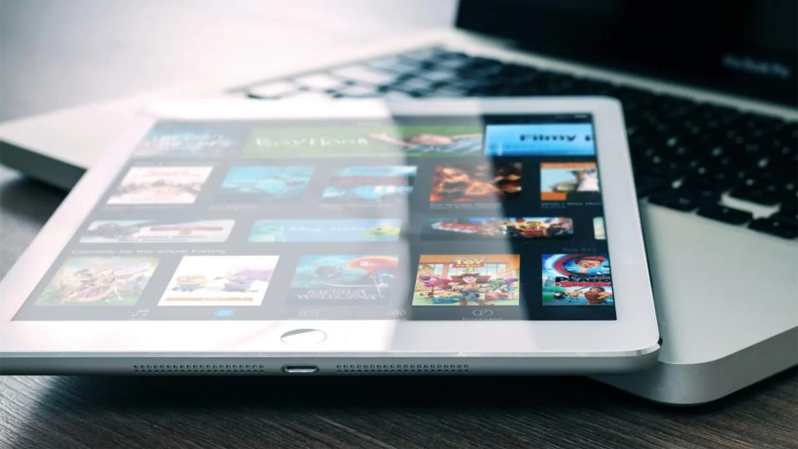 An iPad showing film posters resting on a laptop