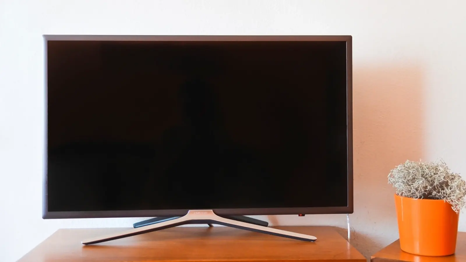 A flat-screen TV on a wooden stand next to a potted plant