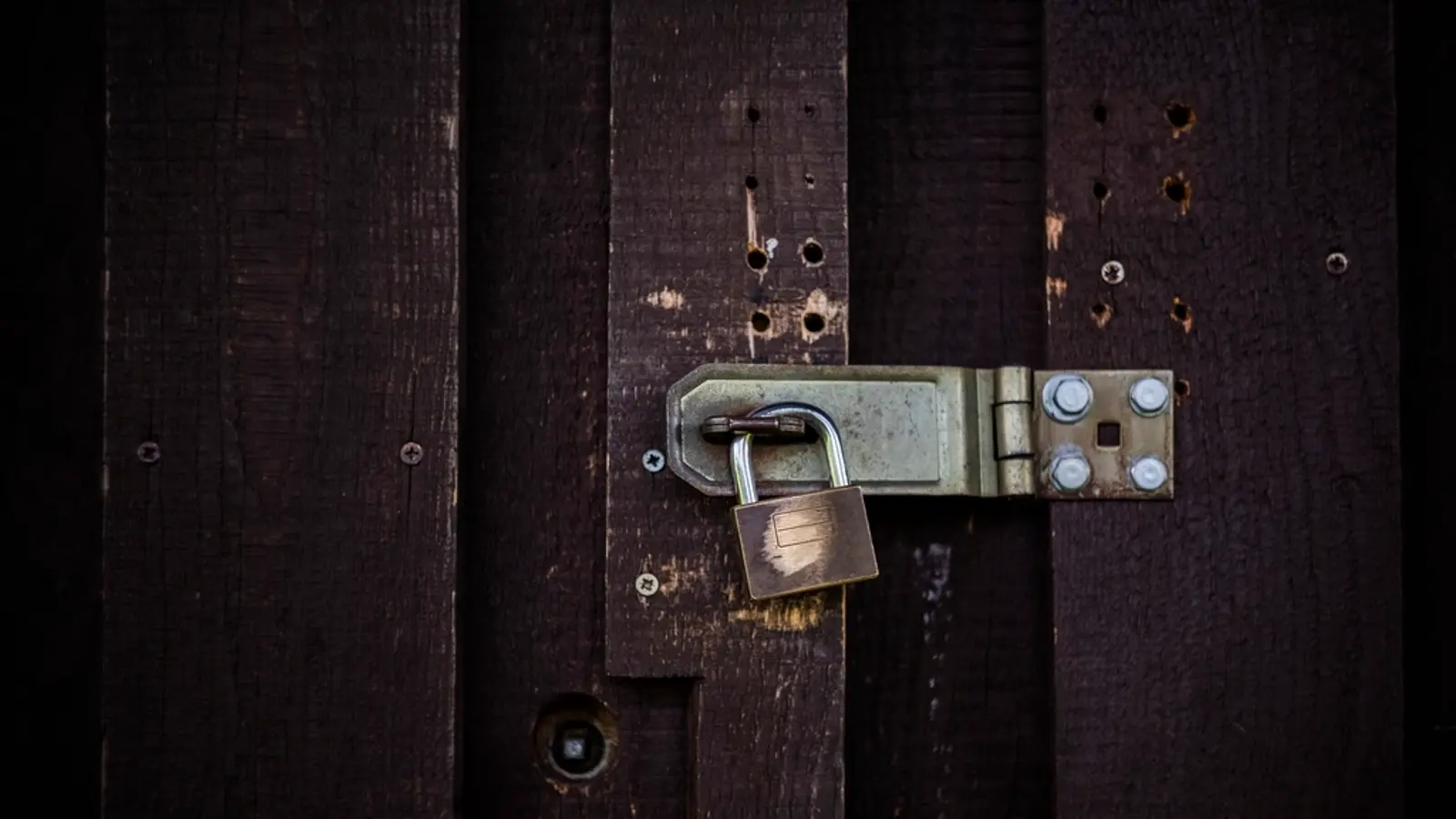 A padlock securing a latch on a dark wooden door