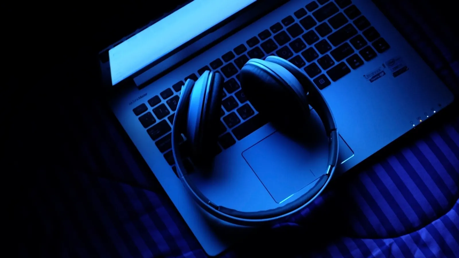 Headphones resting on a laptop keyboard lit in blue